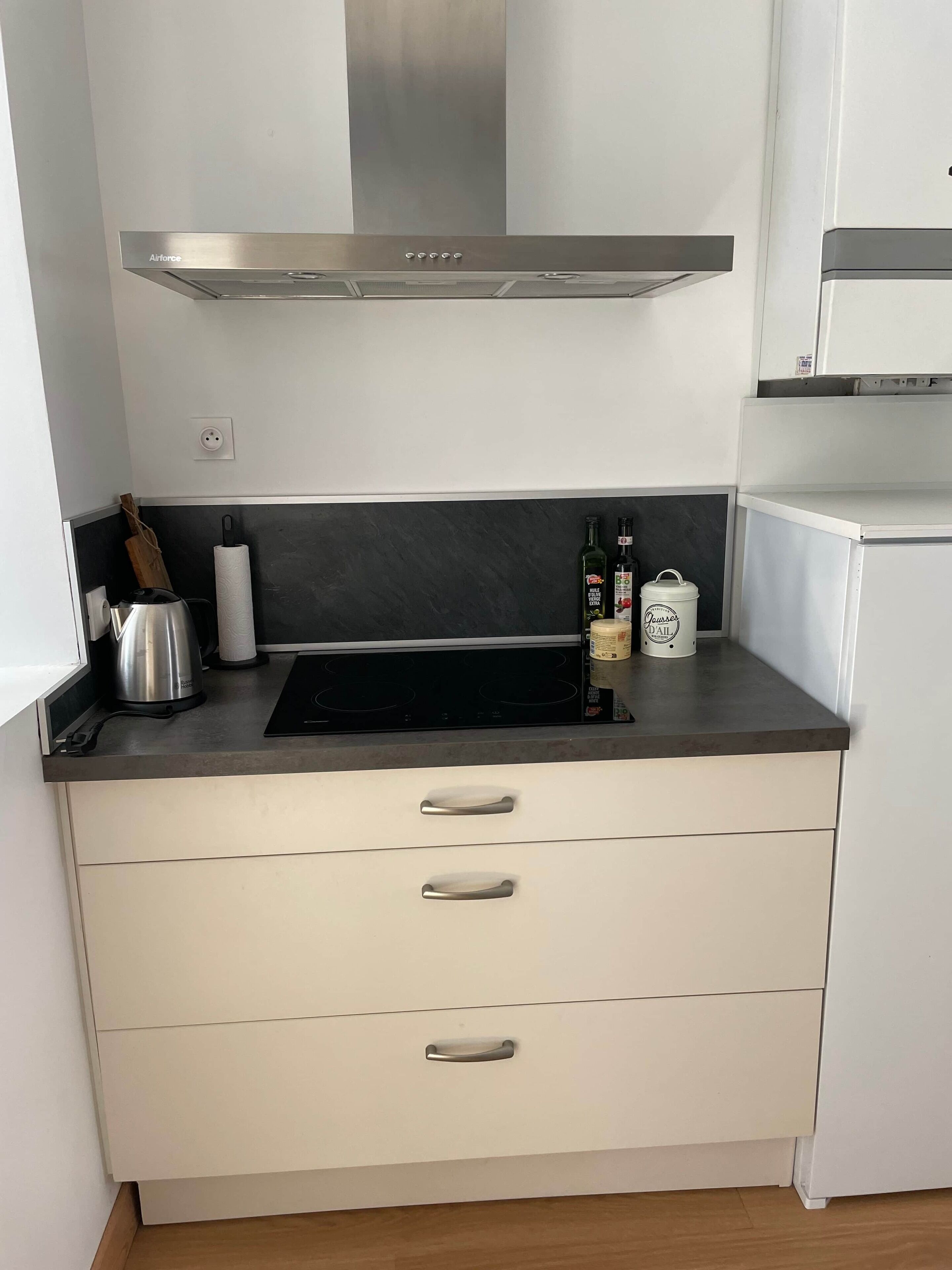 Een keuken met een roestvrijstalen afzuigkap, een zwart inductiekookplaat, een waterkoker en een rol keukentouwen.