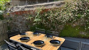 An outdoor dining area with a wooden table and black chairs, set against a stone wall with flowering plants. - Ker Levenez - Stone house Perros-Guirec (Perros-Guirec)
