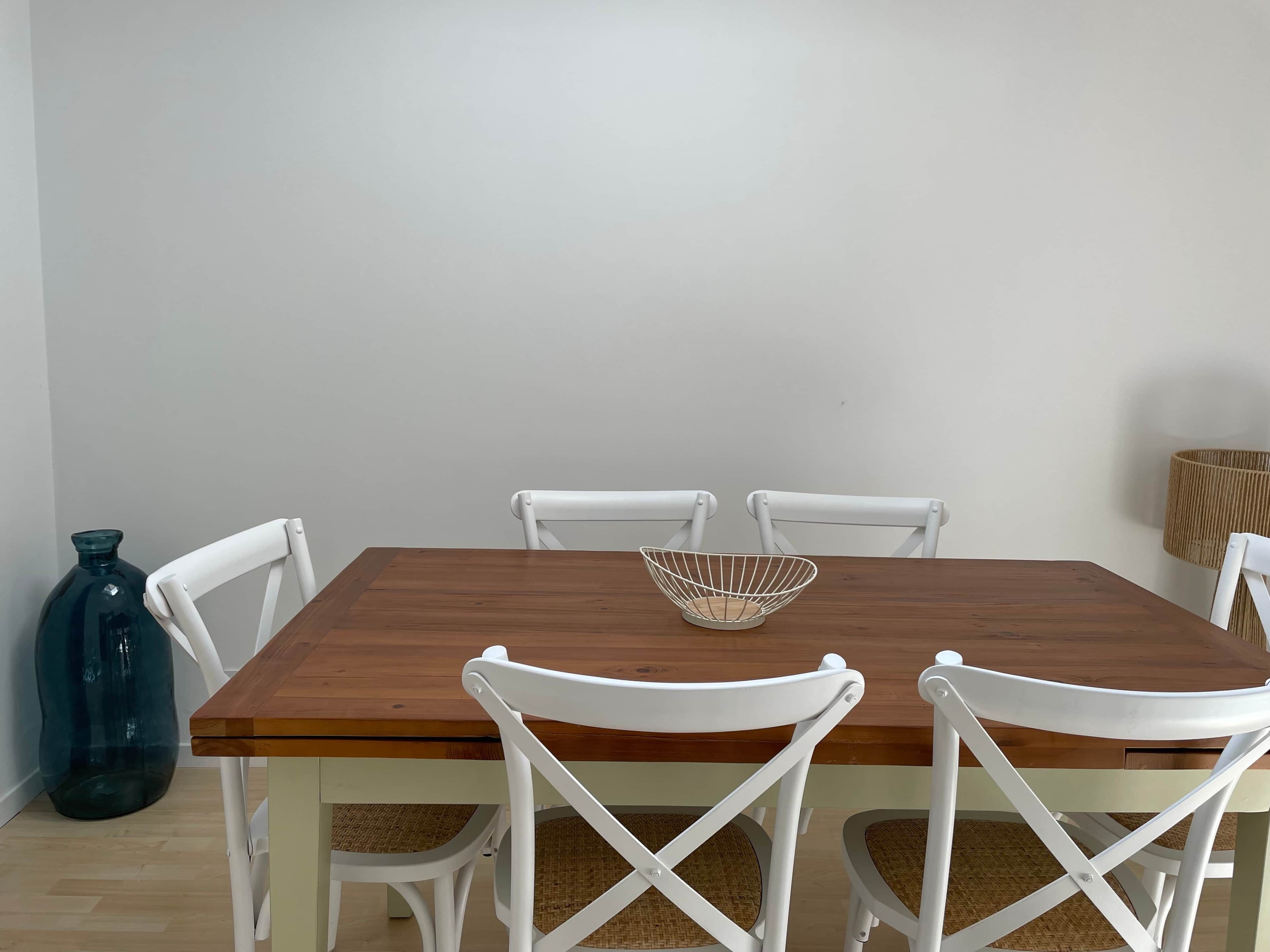 Una mesa de comedor con tapa de madera y sillas blancas con asientos de mimbre.
