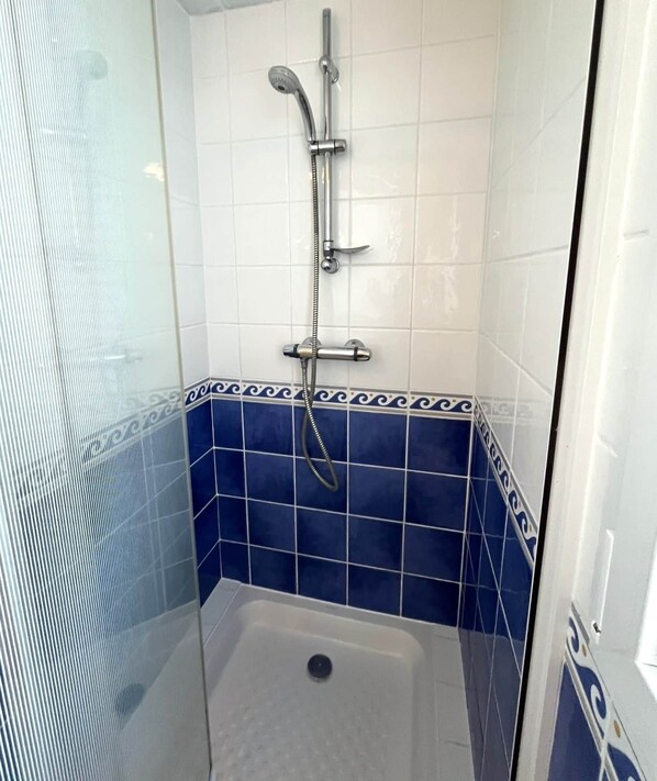 A small, tiled shower area with a handheld showerhead and a wall-mounted faucet.