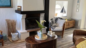 Una sala de estar acogedora con chimenea, un sofá cómodo, una mesita de centro y un sillón de mimbre.