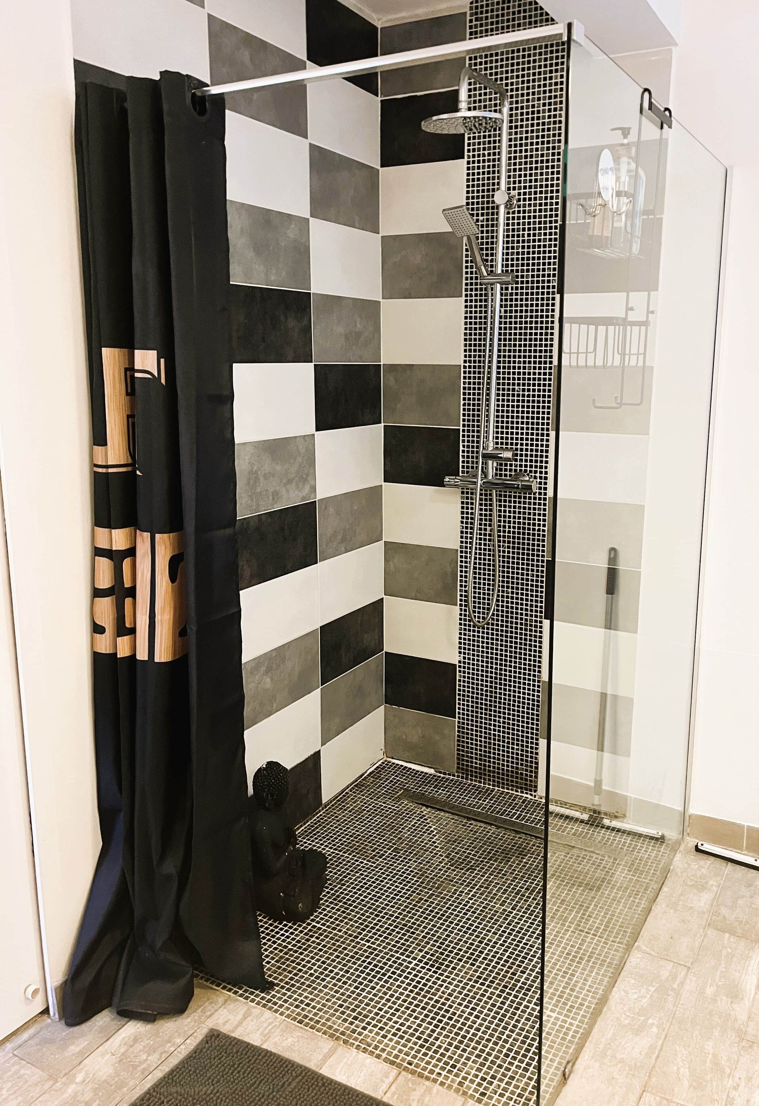 A shower area with a black and white checkered tile wall, a glass shower enclosure, and a black curtain with a geometric pattern.