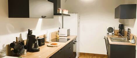 A compact kitchen with a microwave, toaster, and coffee maker on the counter, a sink, and a refrigerator.
