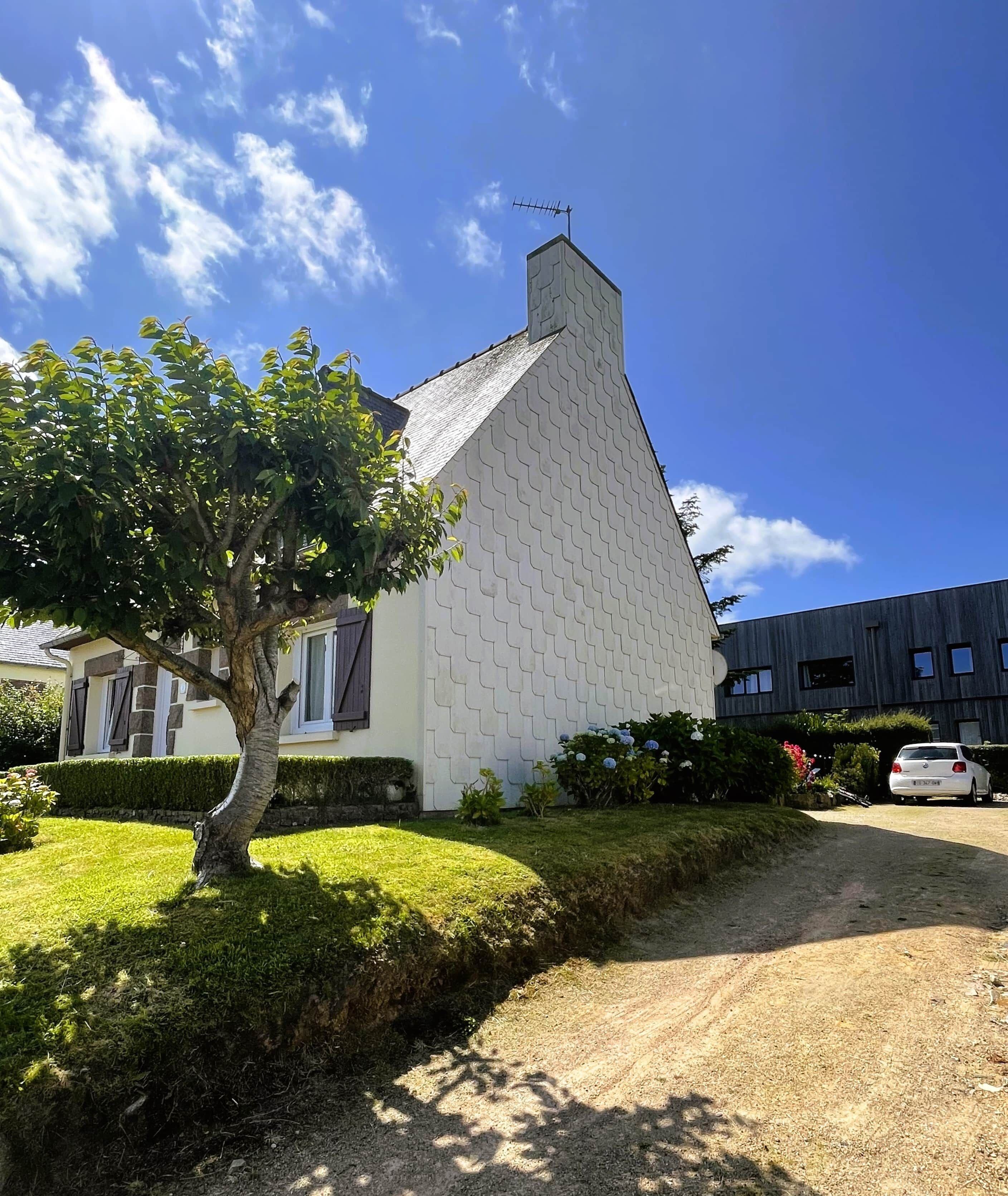 A house with a unique zigzag roof design, a tree in the front yard, and a gravel driveway.