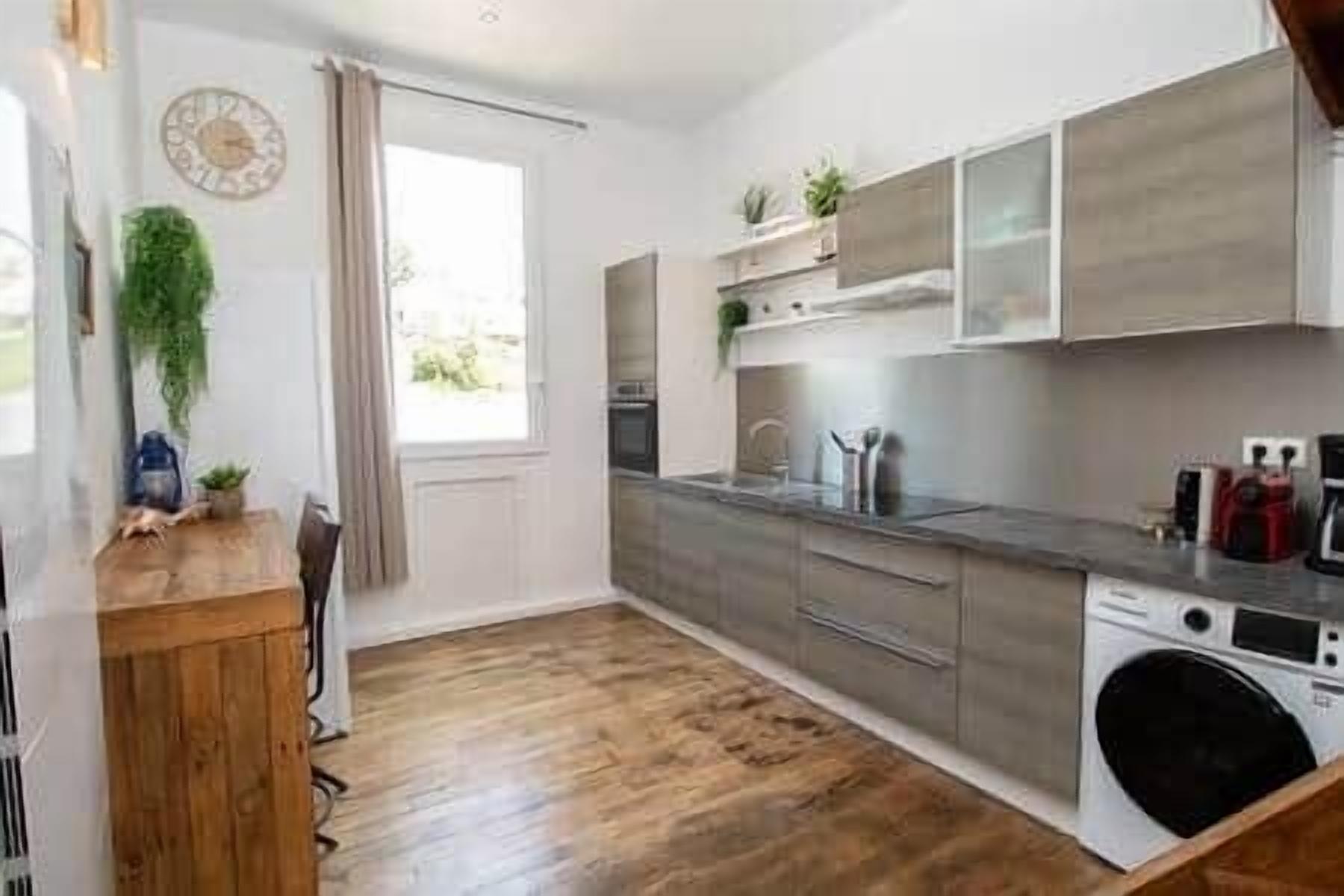 Une cuisine moderne avec un plancher en bois, un lave-linge encastré et une fenêtre avec des rideaux.