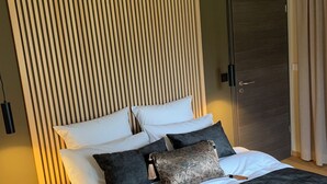 Una habitación de hotel moderna con una cama grande, un cabecero de madera y una puerta oscura.