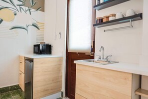Une cuisine compacte avec des meubles en bois, un lave-vaisselle encastré, un évier et une fenêtre avec des stores.