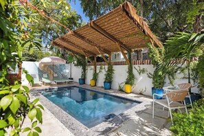 Una piscina con un pérgola de madera, sillas de descanso y plantas en macetas.