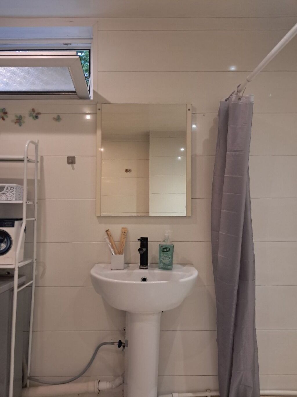 Un bagno con lavandino bianco, specchio, tenda da doccia e porta asciugamani.