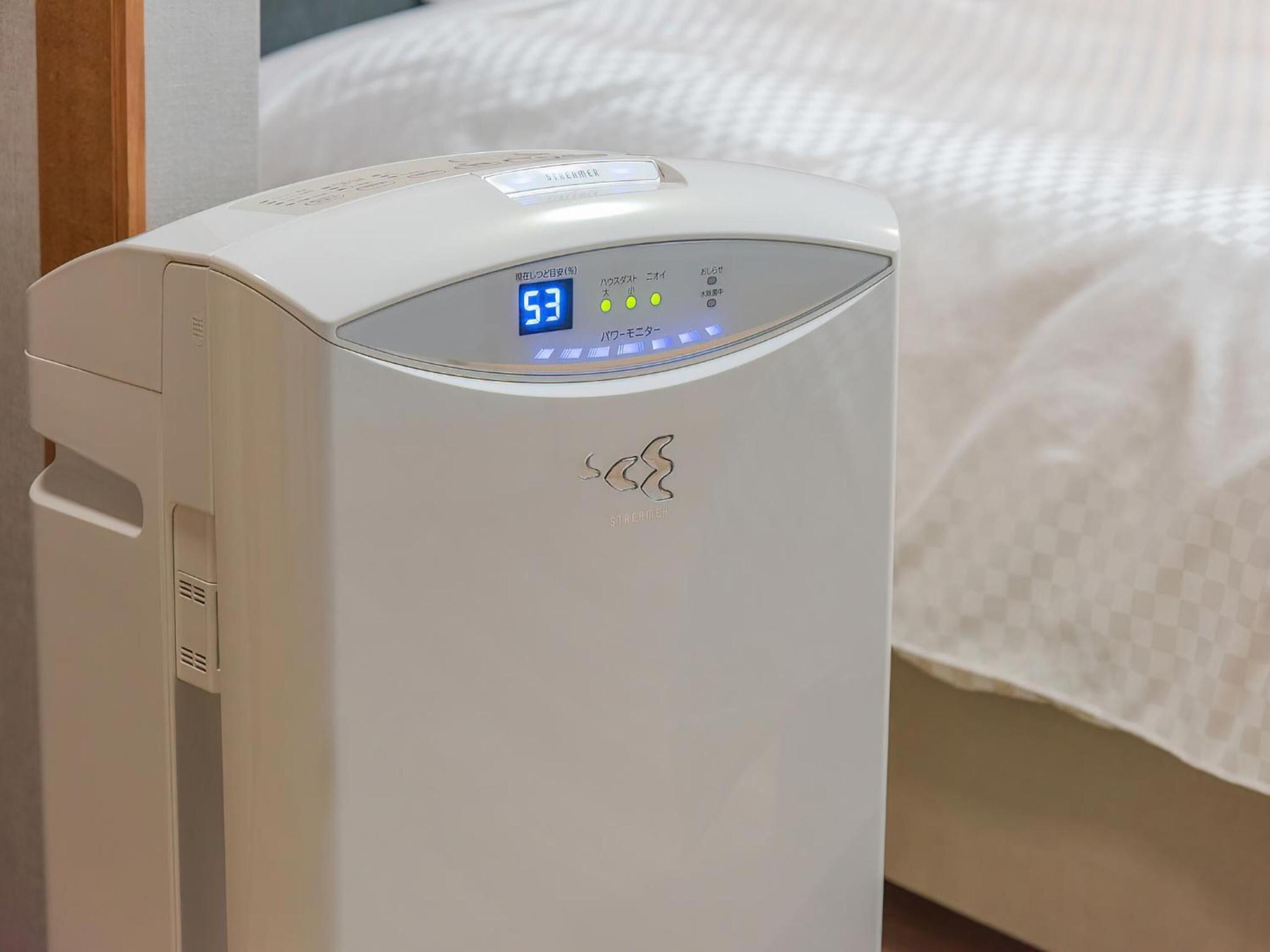 A white portable heater with a digital display, placed in a room with a bed and a wooden door.