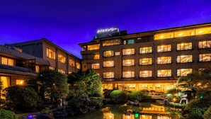 Egy hotel, melynek része egy tükröződő vízfelületű medence, több emeletből áll, és a bejáratánál japán felirat található.