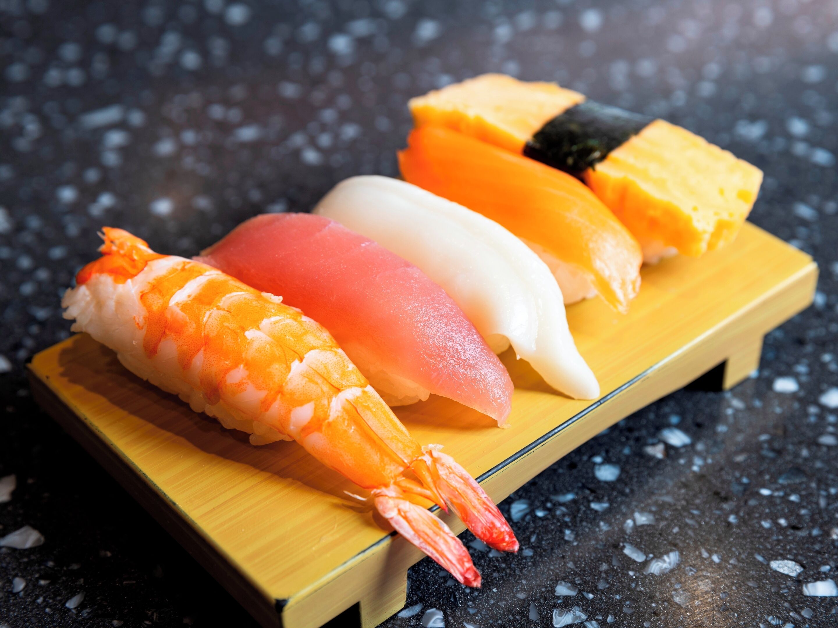 A wooden tray with four pieces of sushi on a dark surface.
