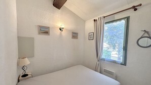 Ein schlichter, sauberer Raum mit Bett, Fenster mit Vorhängen, Wandlampe und Heizkörper.