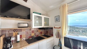 Eine kompakte Küche mit Mikrowelle, Toaster und Kaffeemaschine auf der Arbeitsfläche. Es gibt eine geflieste Spritzschutzleiste und ein Fenster mit Blick auf die Stadt.