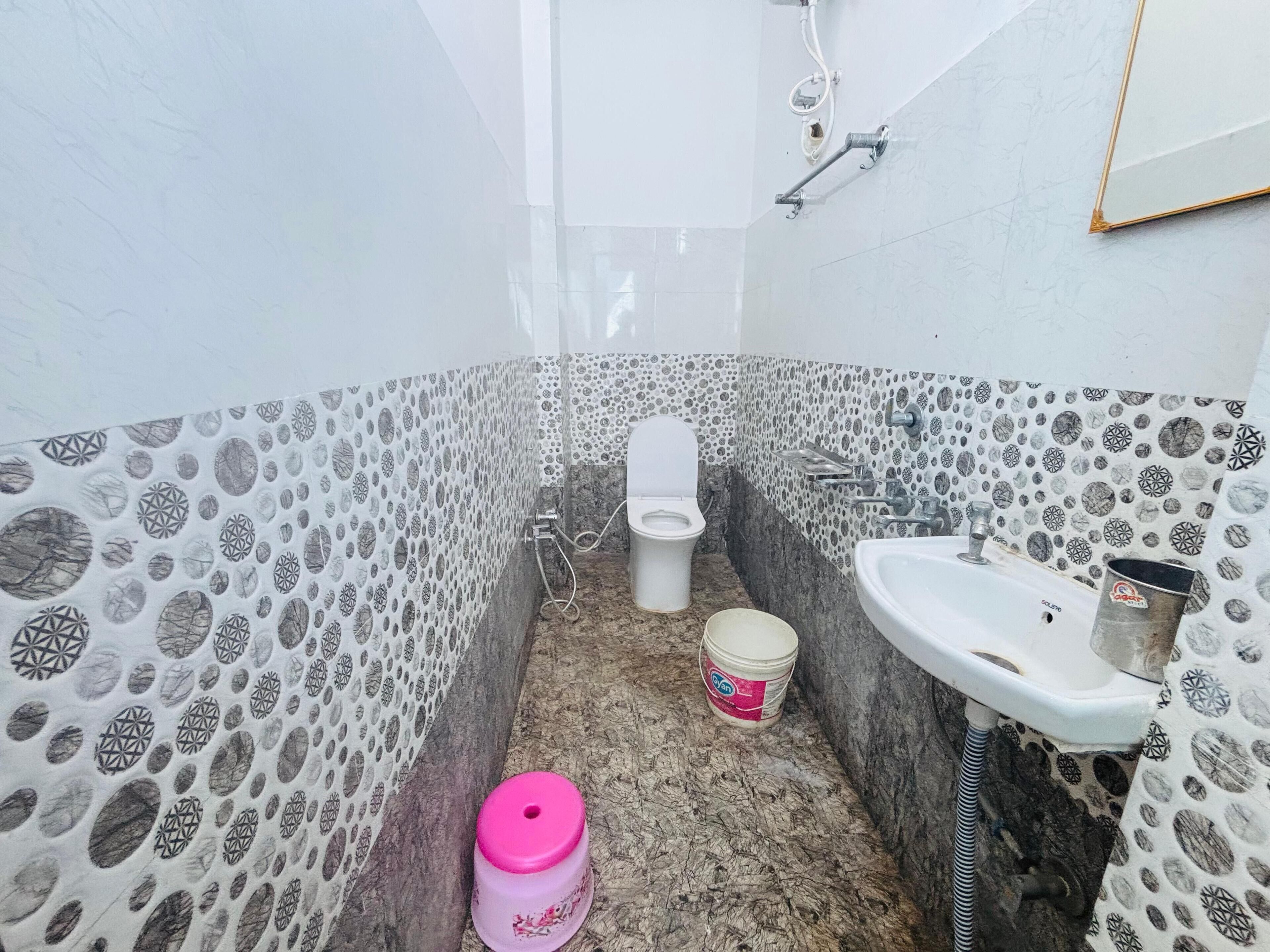 A bathroom with patterned walls, a toilet, a sink, and a bucket.