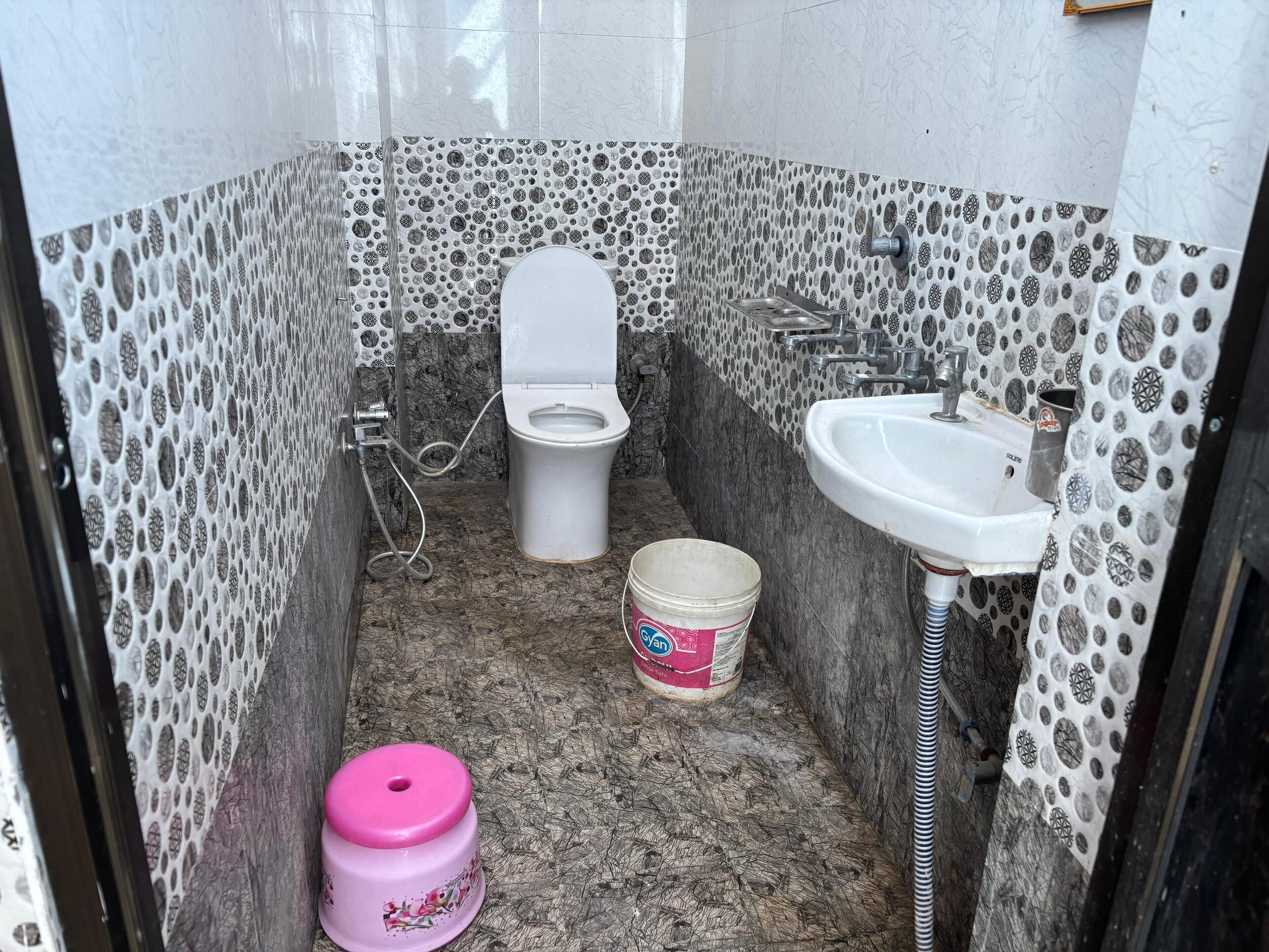 A small, narrow bathroom with a toilet, sink, and a pink stool.