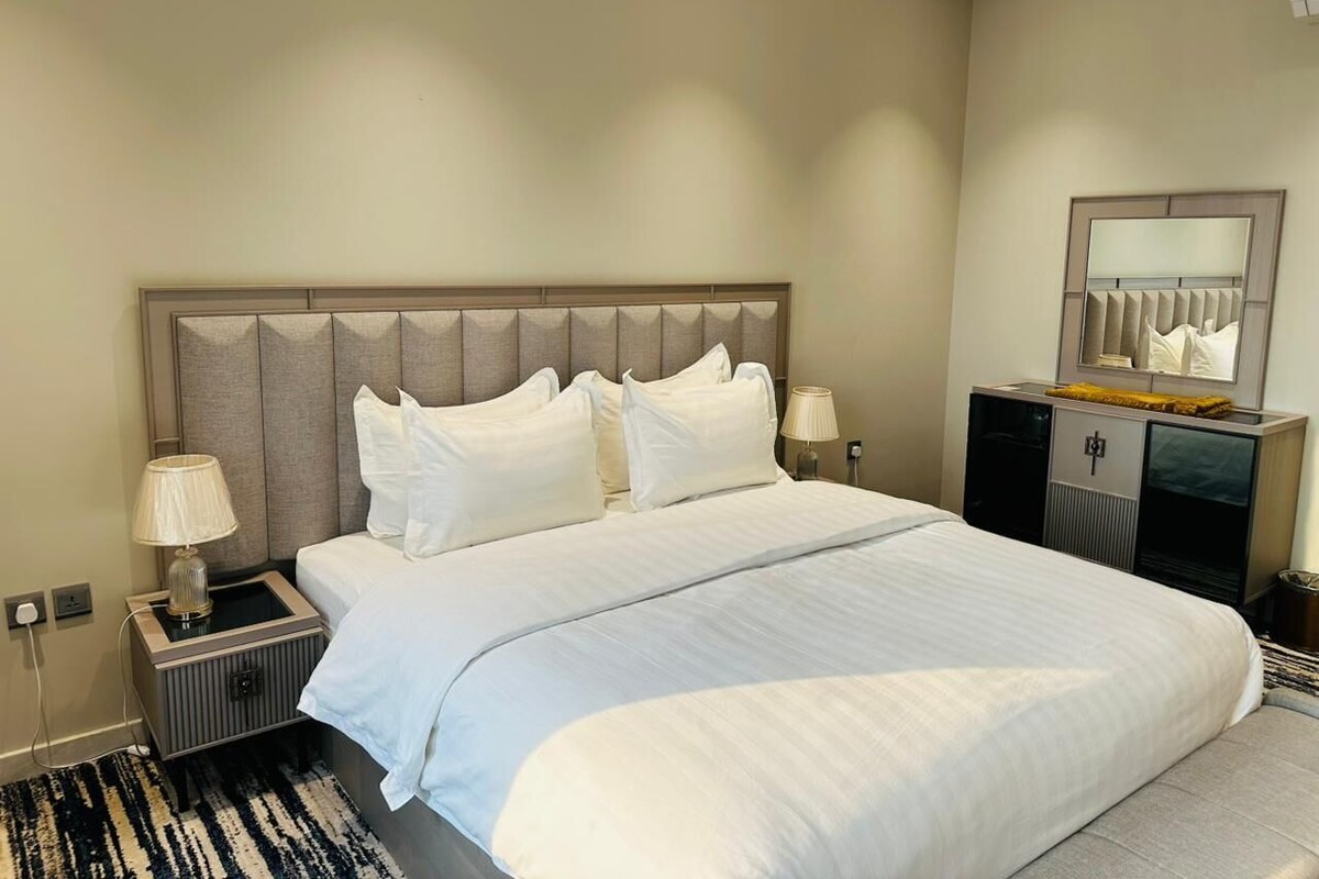 A hotel room with a large bed, two bedside tables with lamps, a dresser, and a mirror on the wall.