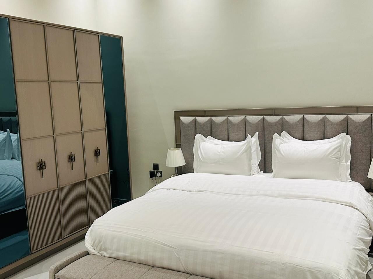 Une chambre d’hôtel avec un grand lit, une armoire et une table de chevet avec une lampe.