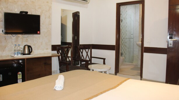 A hotel room with a bed, a desk with a television, a mirror, a shower, and a door. - Flourish Inn Saket opposite Max Hospital (New Delhi)