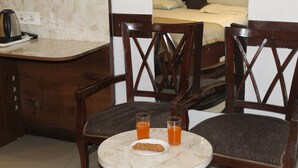 A small room with a round table, two chairs, a bed, and a nightstand with a kettle. - Flourish Inn Saket opposite Max Hospital (New Delhi)