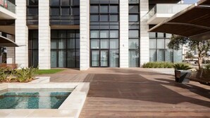 A modern building with large windows, a pool, and a paved courtyard. - Special Apartment Sea View Luxury Tower (Bat Yam)