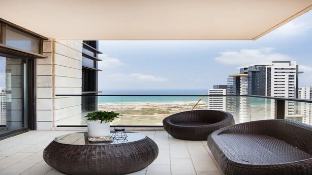A balcony with wicker furniture, a potted plant, and a view of the beach and cityscape. - Special Apartment Sea View Luxury Tower (Bat Yam)
