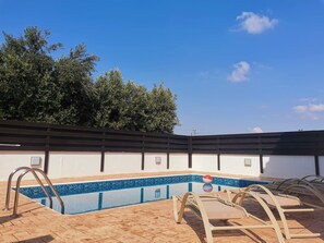 A swimming pool with a tiled edge, surrounded by lounge chairs and a wooden deck. - Minas Villa Pool Wifi and Close to Sirena bay (Paralimni)