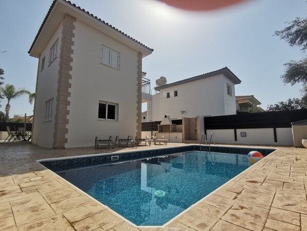 A swimming pool with a tiled deck, a two-story house with a balcony, and a patio area with outdoor furniture. - Minas Villa Pool Wifi and Close to Sirena bay (Paralimni)