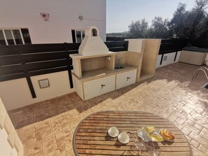 A patio with a round wooden table, a built-in grill, and a sink. - Minas Villa Pool Wifi and Close to Sirena bay (Paralimni)