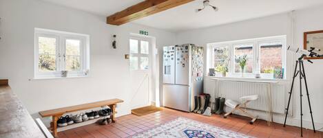 Une cuisine spacieuse avec une grande fenêtre, un banc en bois où sont rangées les chaussures, un tapis à motifs et un trépied.