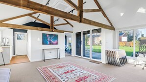A spacious room with a high ceiling, wooden beams, a large window, and a patterned rug. - Guys Head Cottage (Spalding)