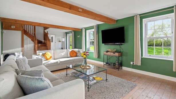 A living room with a white sofa, a glass coffee table, and a flat-screen TV mounted on the wall. - Guys Head Cottage (Spalding)