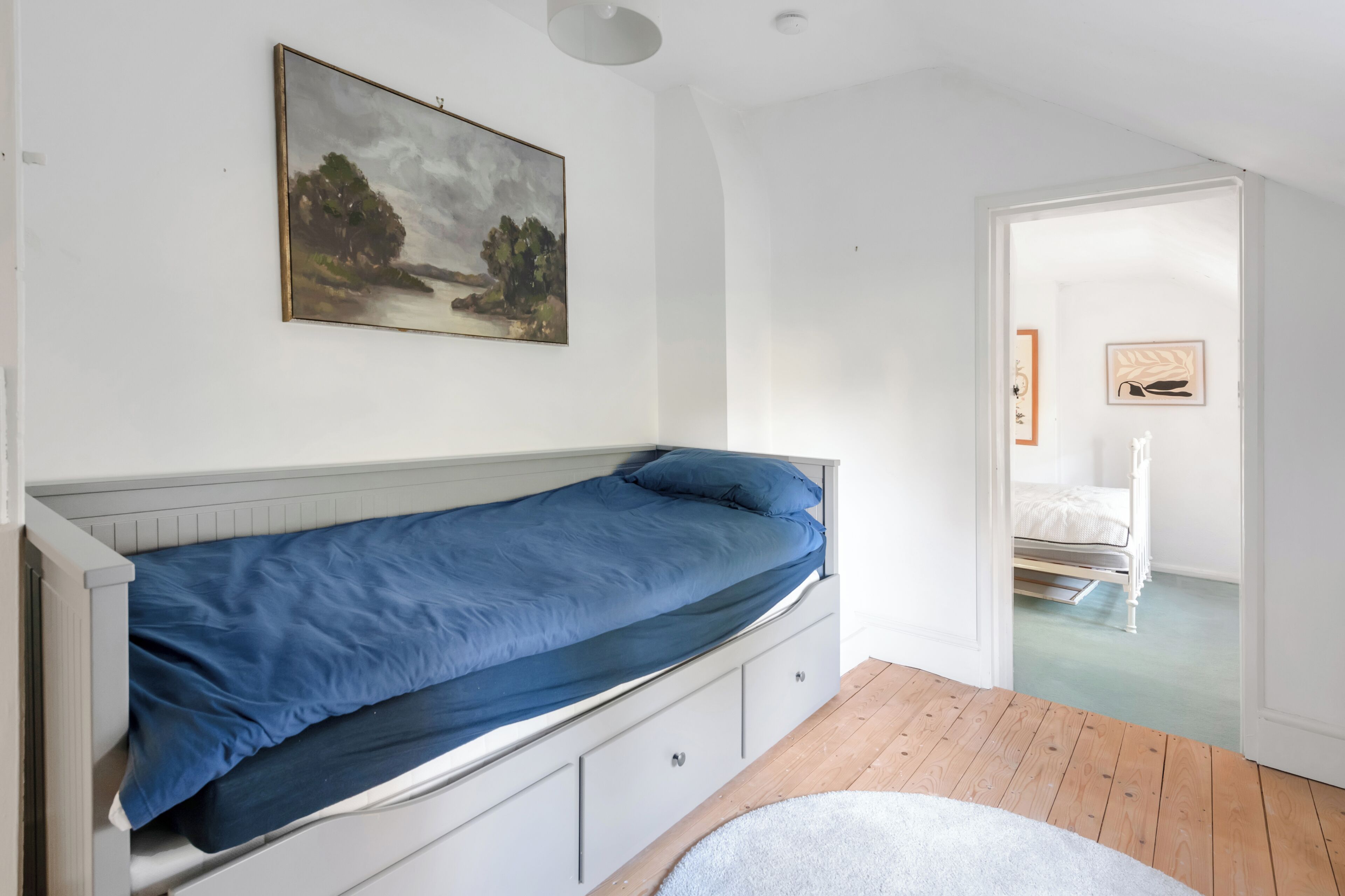 Una cama individual con un colchón azul en una habitación con paredes blancas y piso de madera.