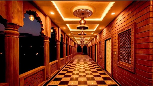 A corridor with checkered flooring, wooden paneling, and decorative ceiling lights. - Umraogarh A Unit of Raghav Vilas (Jodhpur)