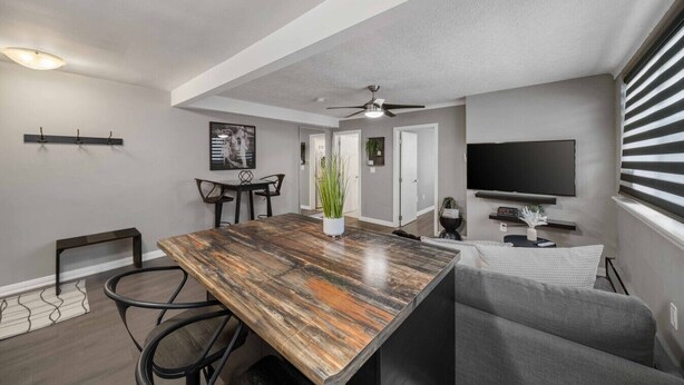 A modern kitchen with a wooden island, black chairs, a dining table, a ceiling fan, and a TV mounted on the wall. - 8 KING Bed, Comfy Sofa, Close To Attractions (Niagara Falls)