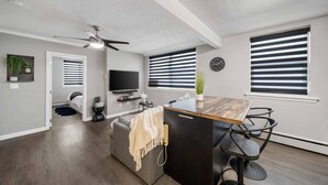 A modern kitchen with a central island, a dining area with chairs, a ceiling fan, and a television mounted on the wall. - 8 KING Bed, Comfy Sofa, Close To Attractions (Niagara Falls)