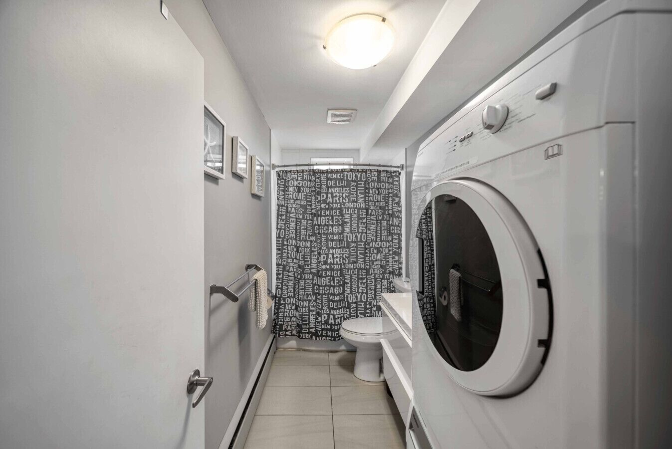 A compact, modern bathroom with a built-in washer and dryer, a toilet, and a wall with city names.