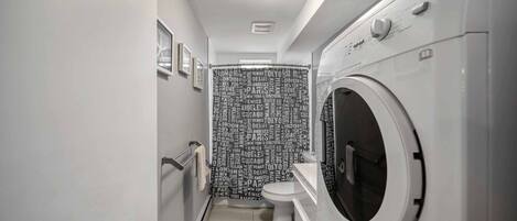A compact, modern bathroom with a built-in washer and dryer, a toilet, and a wall with city names.