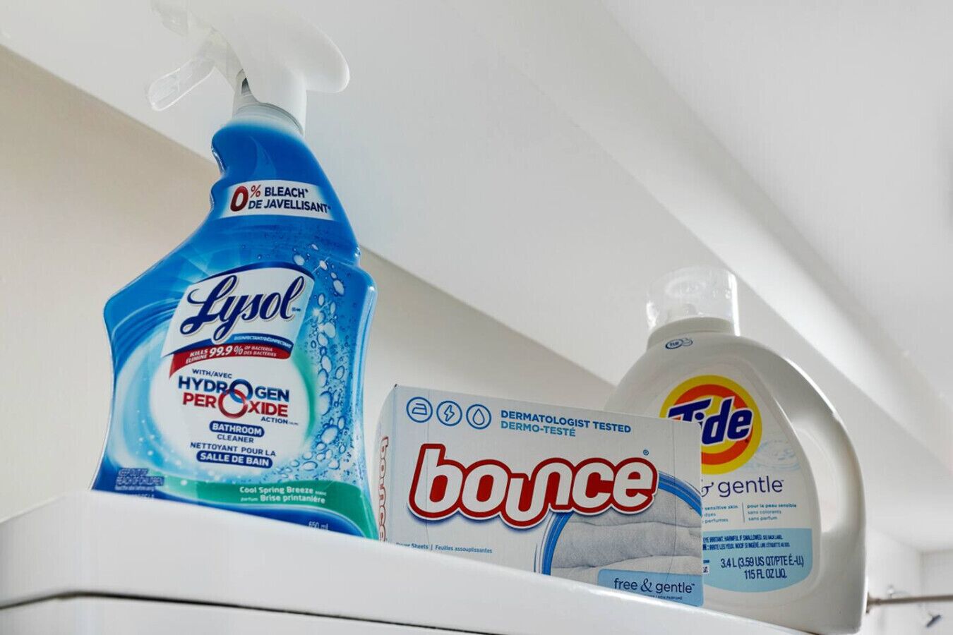 En hylla med en flaska Lysol-rengöringsmedel för badrum, en förpackning med Bounce-sköljmedel och en flaska Tide-tvättmedel.