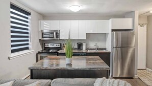 A modern kitchen with white cabinets, stainless steel appliances, and a central island with a plant. - 8 KING Bed, Comfy Sofa, Close To Attractions (Niagara Falls)