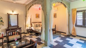 Una habitación tradicional con cama, zona de estar con mesa y sillas, un espejo y un ventilador decorativo en el techo.