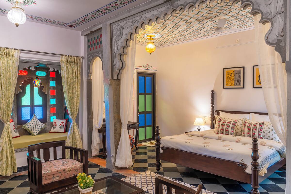 A traditional room with a bed, a window with curtains, a chair, and a table with a plant.