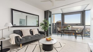 Een moderne woonkamer met een grijze bank, een ronde salontafel en een eethoek met uitzicht op de stad.