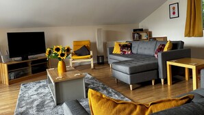 Un salon moderne avec un téléviseur à écran plat, un canapé, une table basse et une bibliothèque.