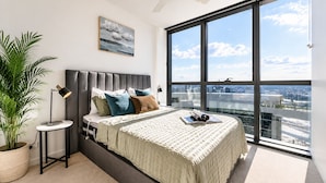 Ein modernes Schlafzimmer mit einem großen Bett, einem Deckenventilator, Blick auf die Stadt und einer Topfpflanze.