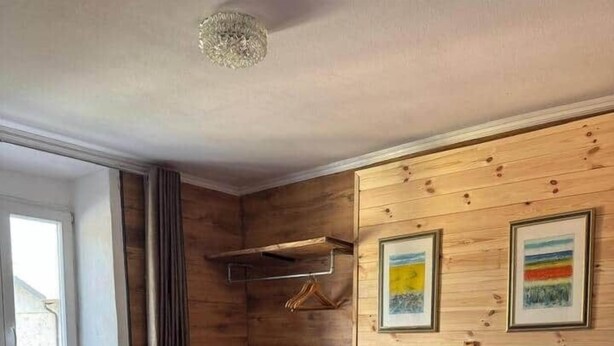Une chambre à coucher avec un lit, des oreillers, une tête de lit, une fenêtre, des rideaux, un mur en bois et deux tableaux encadrés.