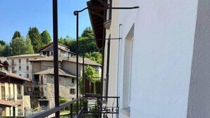 Un balcon étroit doté d’une rambarde en métal, une petite fenêtre et une vue sur les bâtiments voisins et la verdure.