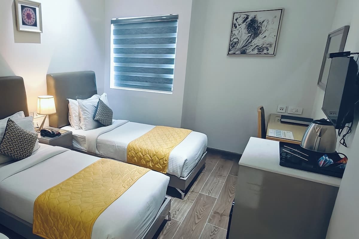 Ein Hotelzimmer mit zwei Betten, einem Schreibtisch, einem Stuhl, einem Fernseher und einem Fenster mit Jalousien.