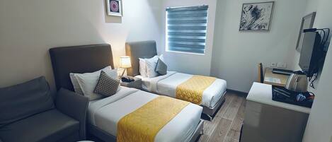 A hotel room with two beds, a desk, a chair, a TV, and a window with blinds.