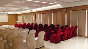 A conference room with rows of chairs, some covered in white and others in red, and a large screen at the front. - The Mayberry A Bergamont Hotel Tiruppur (Tirupur)